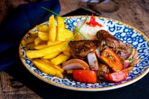 Colorful Lomo Saltado served with crispy fries and rice on a decorative plate.